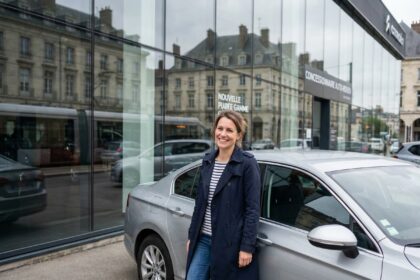 Femme souriante en trench et jeans devant une voiture à Rouen