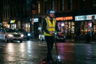 Homme en trottinette électrique la nuit avec gilet réfléchissant et lumières LED sur rue urbaine mouillée